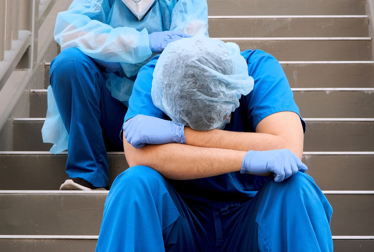 Overworked health care workers wearing protective face masks very sad sitting on the stairs (Getty Images/Juanmonino)