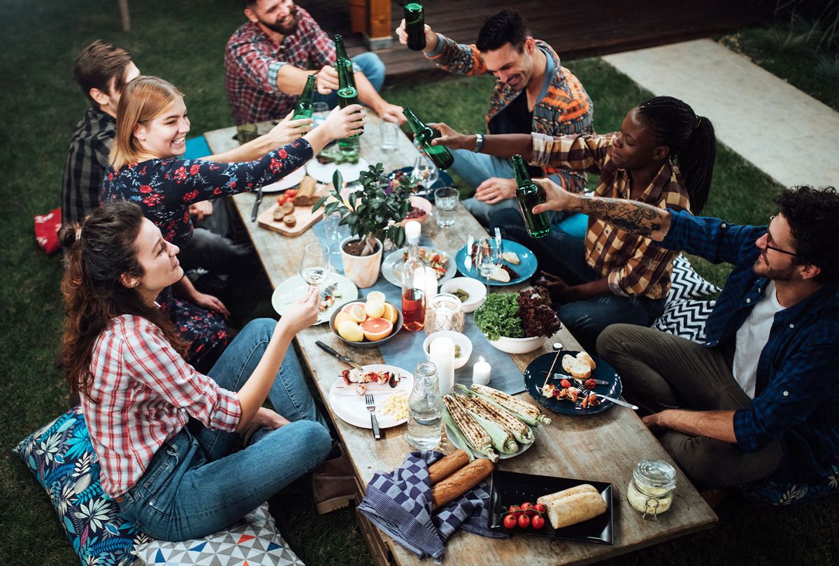 Friends toasting with wine and beer at a rustic dinner party (Getty Images/Anchiy)