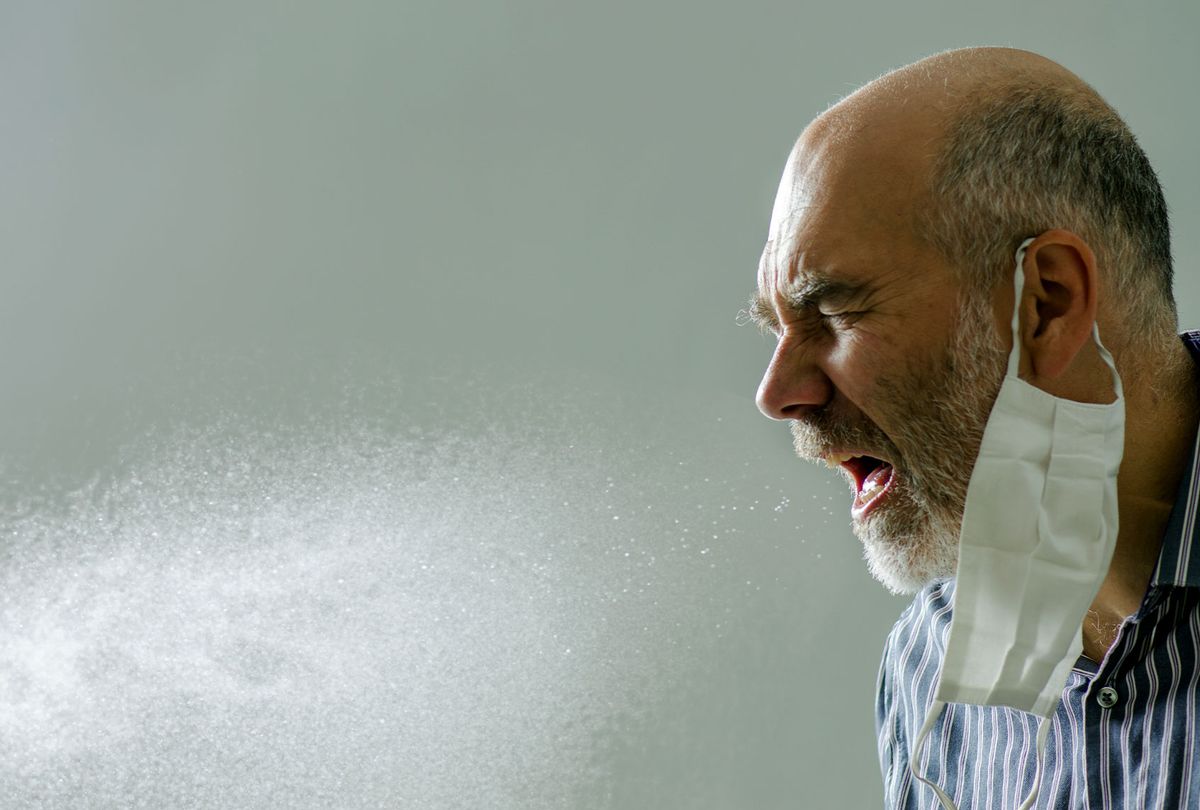 Man sneezing with spray of water droplet full of virus or microbes. He wears his face mask inappropriately on one ear.
 (Getty Images/Marc Dufresne)