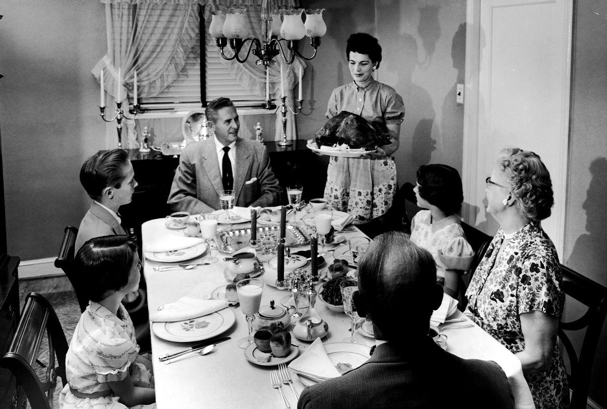 A family sits at a formally prepared dinner table, looking eager as a woman brings a roast turkey to the table on a platter, 1950s. (Lambert/Getty Images)