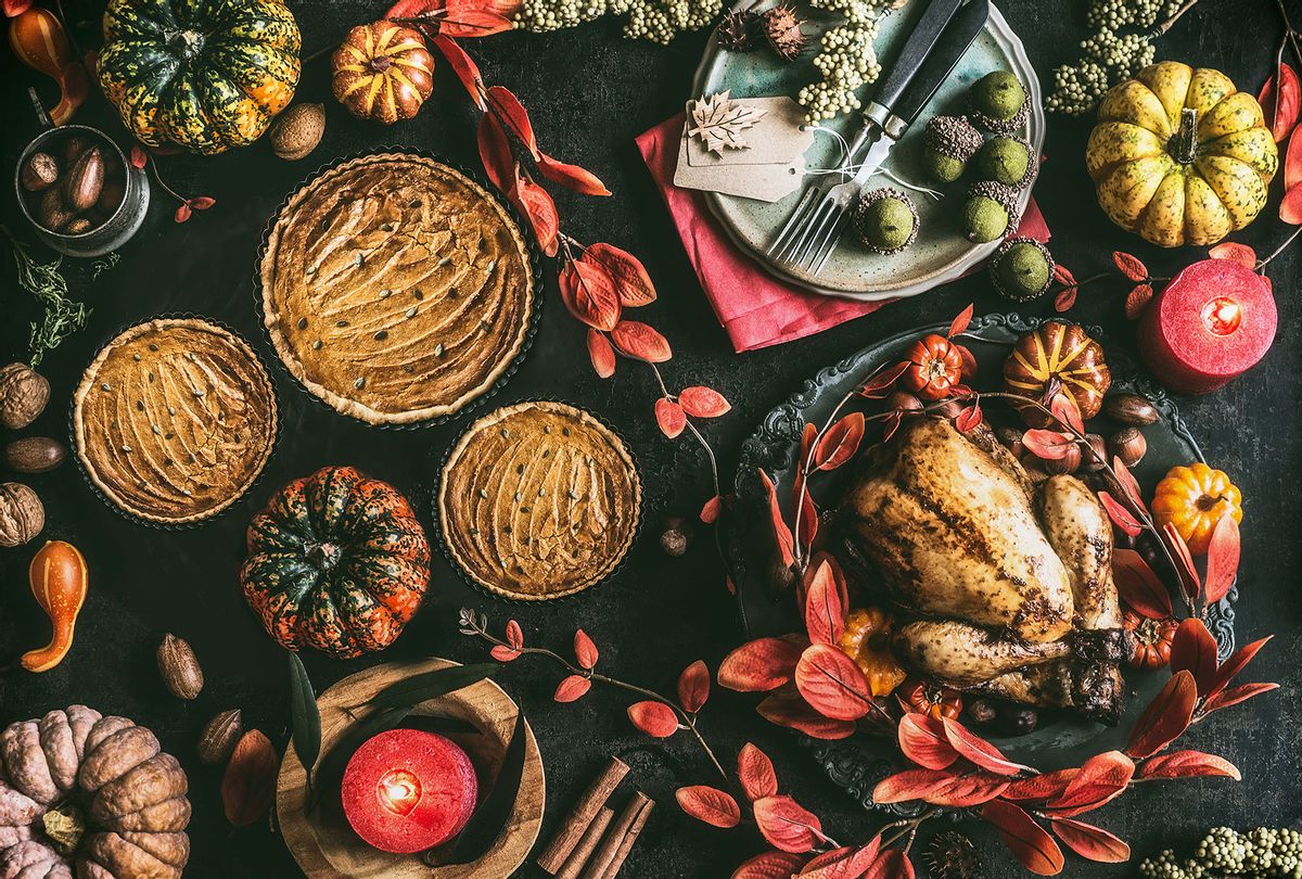 Thanksgiving day dinner table with roasted whole chicken or little turkey , pumpkin pie on dark rustic background with plates, sauce, cutlery, burning candles, red autumn leaves, nuts and festive decoration (Getty Images/VICUSCHKA)