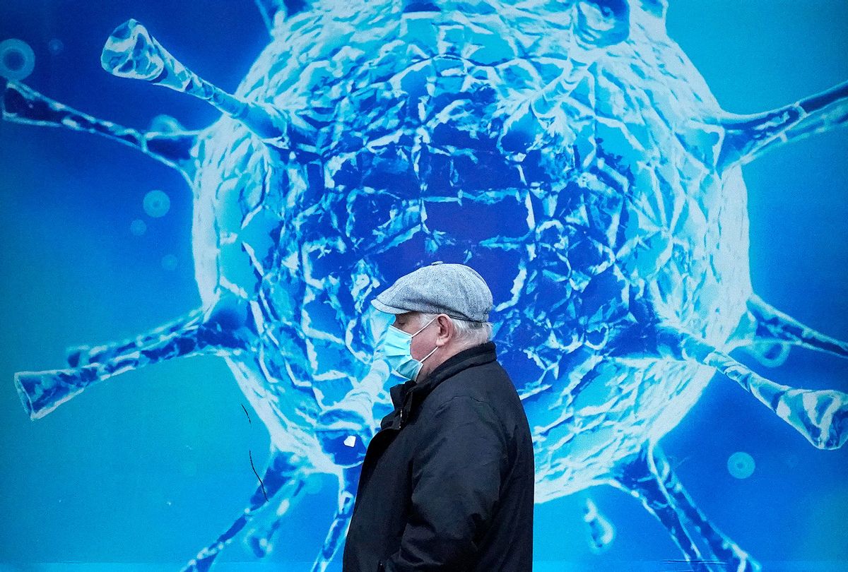 A man wearing a protective face mask walks past an illustration of a virus outside Oldham Regional Science Centre on November 24, 2020 in Oldham, United Kingdom. (Christopher Furlong/Getty Images)