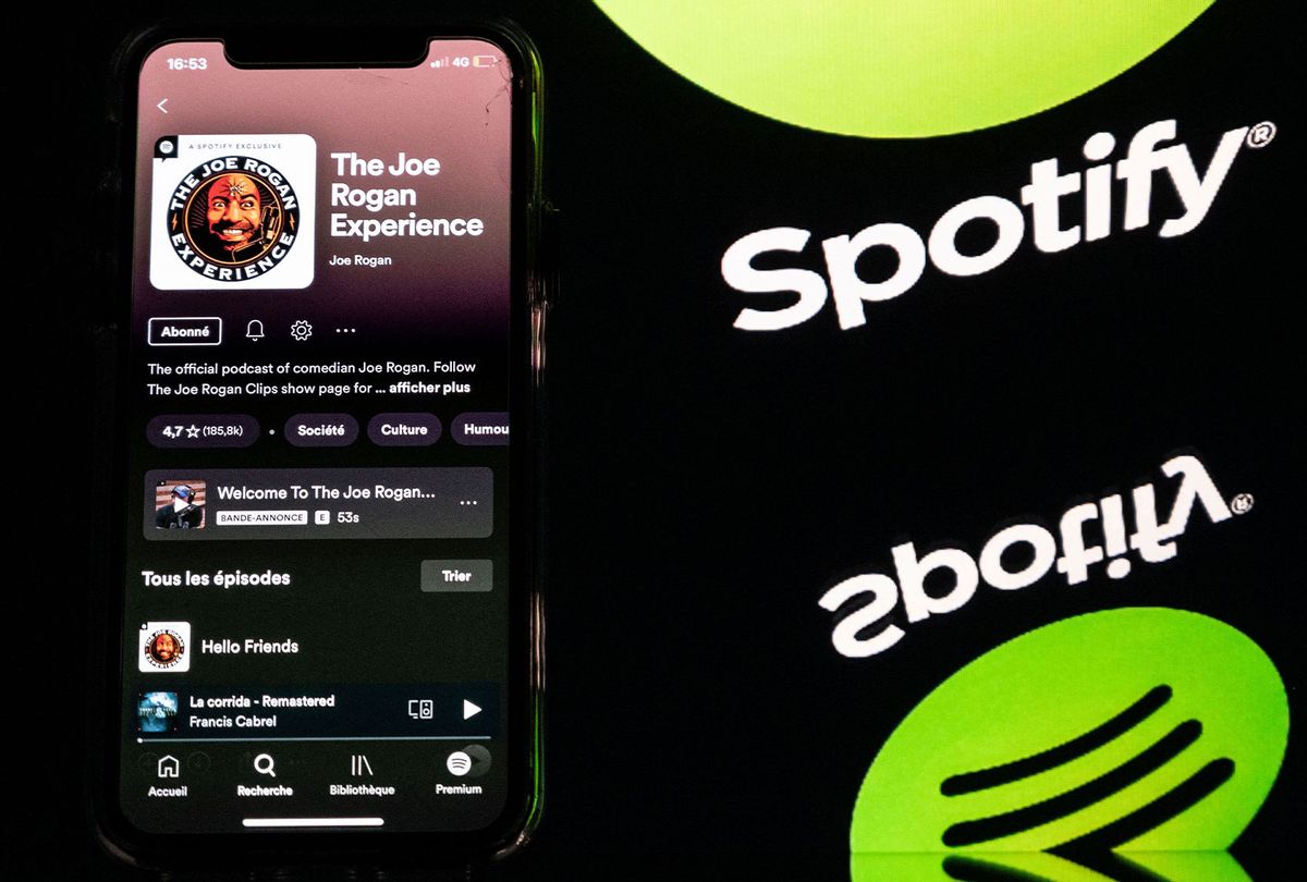 A smartphone displaying the Joe Rogan podcast and a screen displaying the Spotify's logo. (LIONEL BONAVENTURE/AFP via Getty Images)