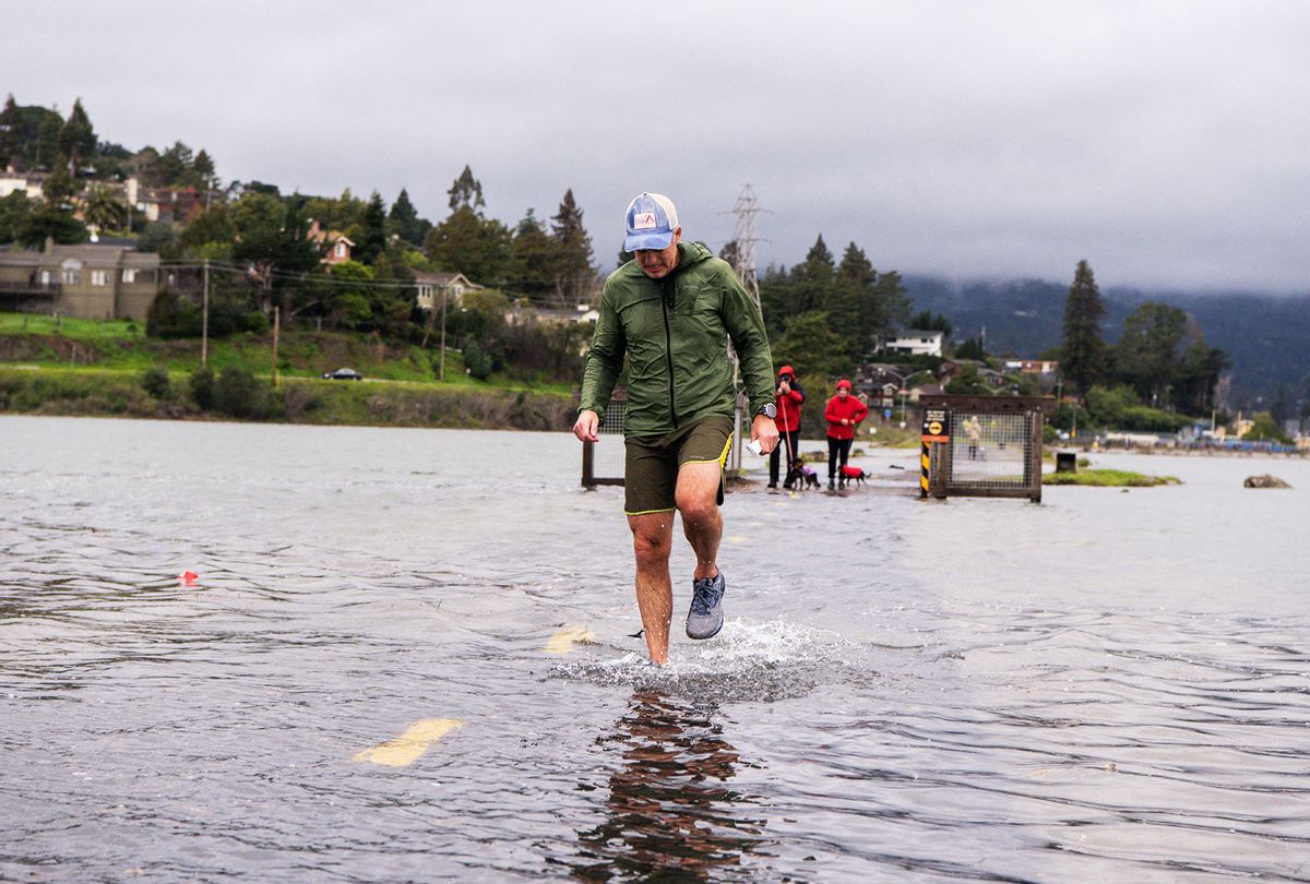 A jogger makes his way along a flooded Sausalito/Mill Valley bike path during the "King Tide" in Mill Valley, California on Jananury 3, 2022. - "King Tides" occur when the Earth, moon, and sun align in orbit to produce unusually high water levels and can cause local tidal flooding. Over time, sea level rise is raising the height of tidal systems. (JOSH EDELSON/AFP via Getty Images)