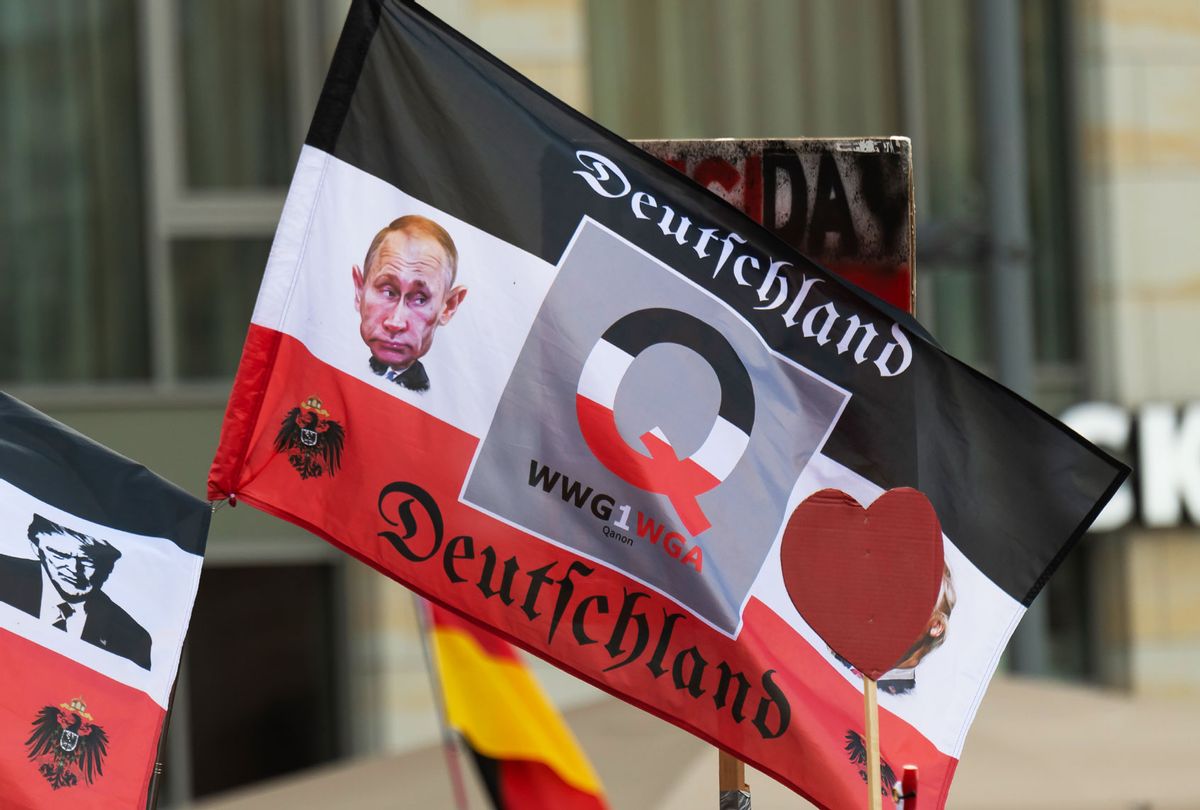 Participants display Qanon flags at an event marking the 7th anniversary of the Pegida movement. The flag features the head of Russian President Putin, the Q for "Qanon" and the letter abbreviation WWG1WGA ("Where we go one we go all"). Meaning "Where one of us goes, we all go", or "One for all, all for one". With this, the Qanon followers evoke the cohesion of their community. (Matthias Rietschel/picture alliance via Getty Images)
