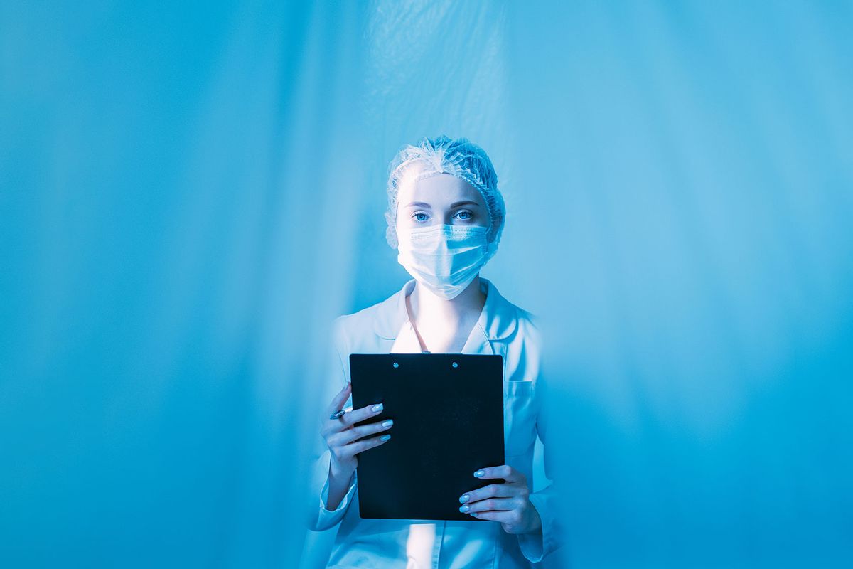 Female doctor with clipboard isolated with blue plastic drapes (Getty Images/golubovy)