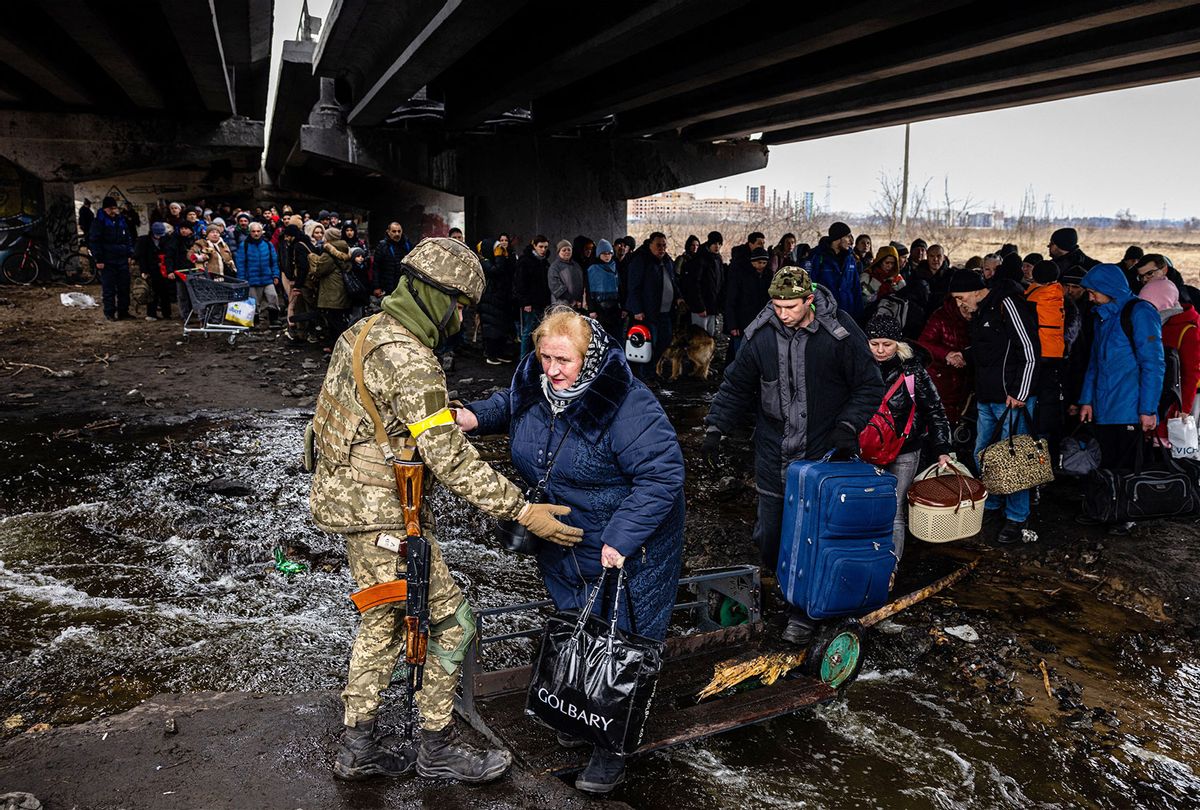 A Ukrainian serviceman helps evacuees gathered under a destroyed bridge, as they flee the city of Irpin, northwest of Kyiv, on March 7, 2022. - Ukraine dismissed Moscow's offer to set up humanitarian corridors from several bombarded cities on March 7, 2022, after it emerged some routes would lead refugees into Russia or Belarus. The Russian proposal of safe passage from Kharkiv, Kyiv, Mariupol and Sumy had come after terrified Ukrainian civilians came under fire in previous ceasefire attempts. (DIMITAR DILKOFF/AFP via Getty Images)