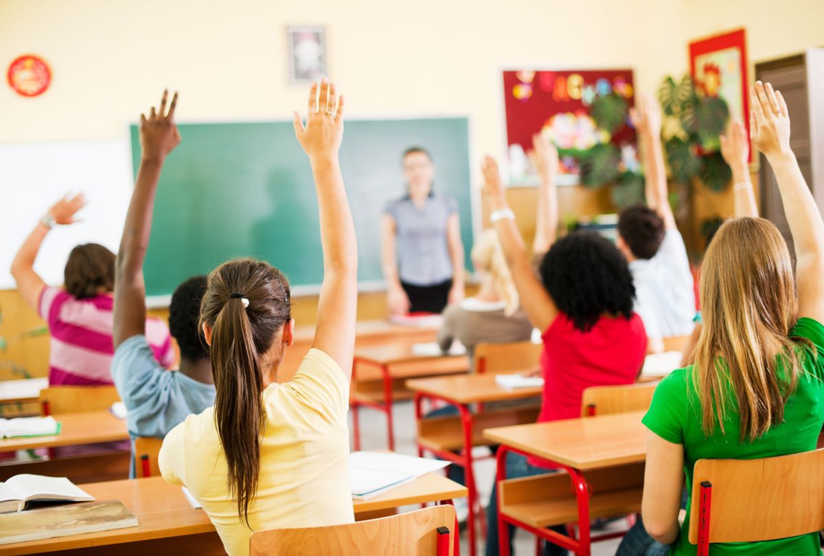 Students sitting in a classroom and raising hands (Getty Images / skynesher)
