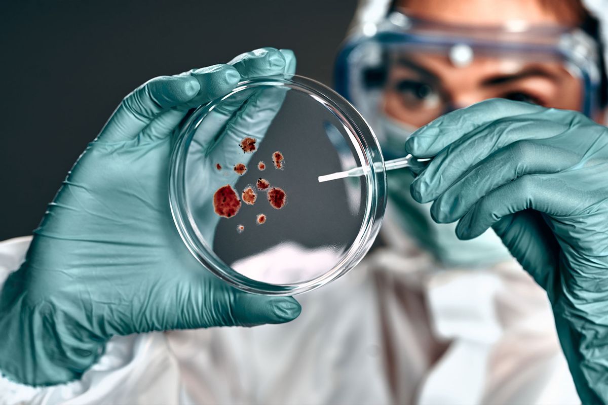 Biochemist in hazmat suit holding petri dish with biomaterial (Getty Images/Harbucks)