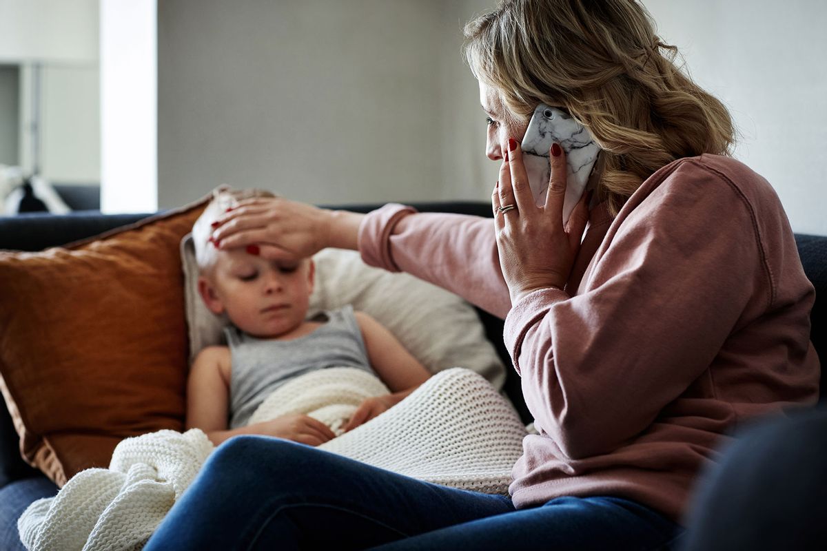 Mother making a phone call while aiding to her sick young son at home (Getty Images/Dean Mitchell)