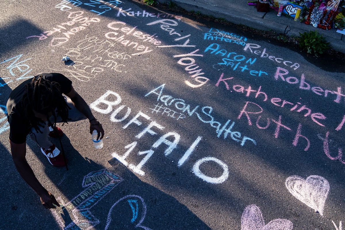 Aaron Jordan, of Buffalo, adds to a sidewalk chalk mural depicting the names of the people killed yesterday as people gather at the scene of a mass shooting at Tops Friendly Market at Jefferson Avenue and Riley Street on Sunday, May 15, 2022 in Buffalo, NY. (Kent Nishimura / Los Angeles Times via Getty Images)