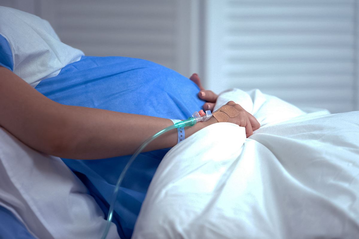 Pregnant woman in a hospital bed holding a blanket, feeling abdominal pain, risk of miscarriage (Getty Images/Motortion)