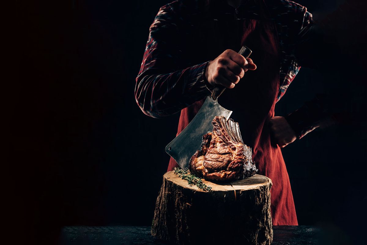 Chef in apron holding meat knife and delicious grilled ribs on wooden stump (Getty Images/LightFieldStudios)