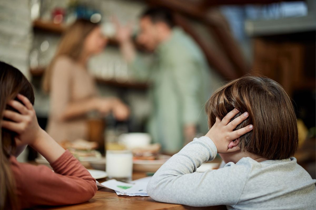 Small siblings covering their ears while refusing to listen their parents arguing in dining room (Getty Images/skynesher)