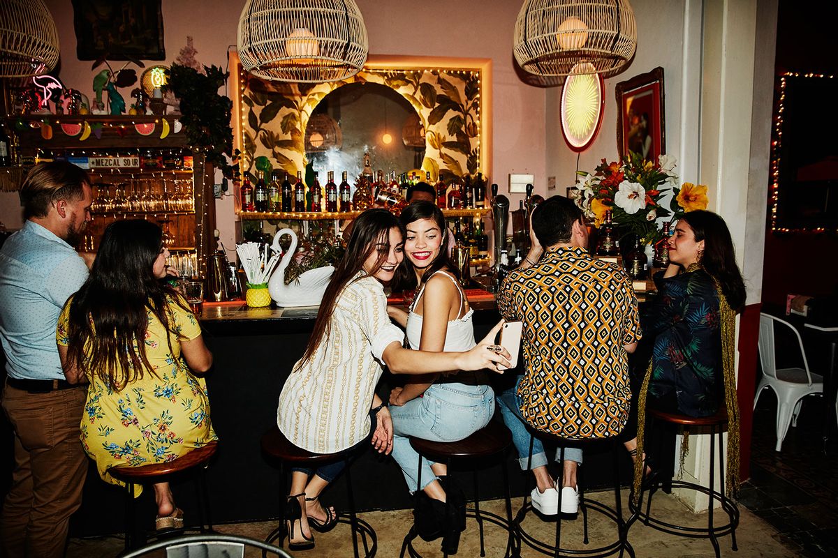 Female friends taking selfie with smart phone while sitting at bar (Getty Images/Thomas Barwick)