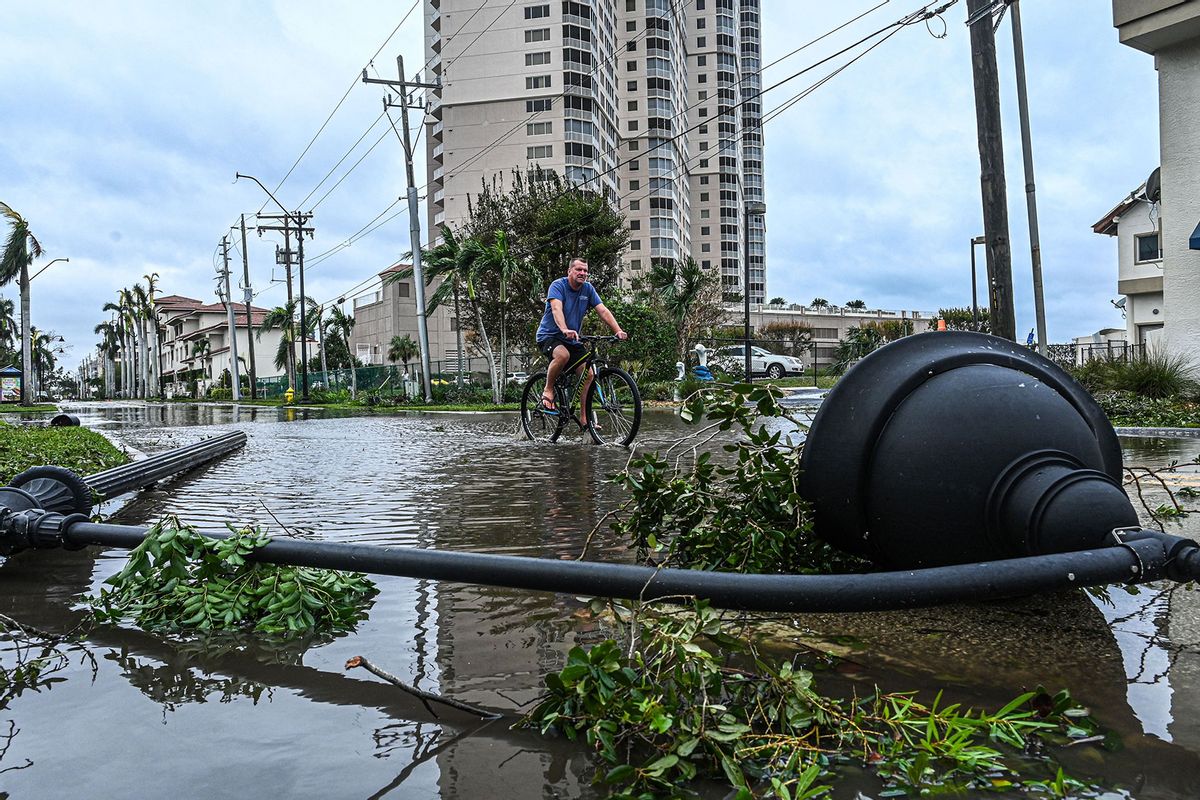 A man cycles through water past a downed street lamp in the aftermath of Hurricane Ian in Fort Myers, Florida, on September 29, 2022. (GIORGIO VIERA/AFP via Getty Images)