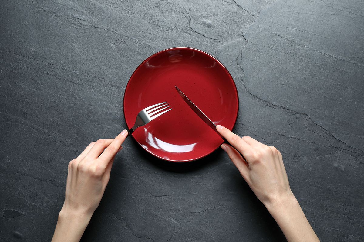 Woman with fork, knife and empty plate at black table (Getty Images/Liudmila Chernetska)