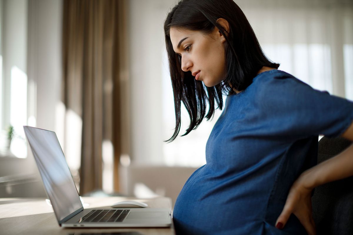 Young pregnant woman sitting in front of her laptop (Getty Images/damircudic)