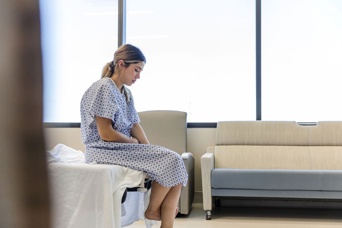 The anxious, sad, young female patient wears her gown as she waits in the hospital room (Getty Images/SDI Productions)