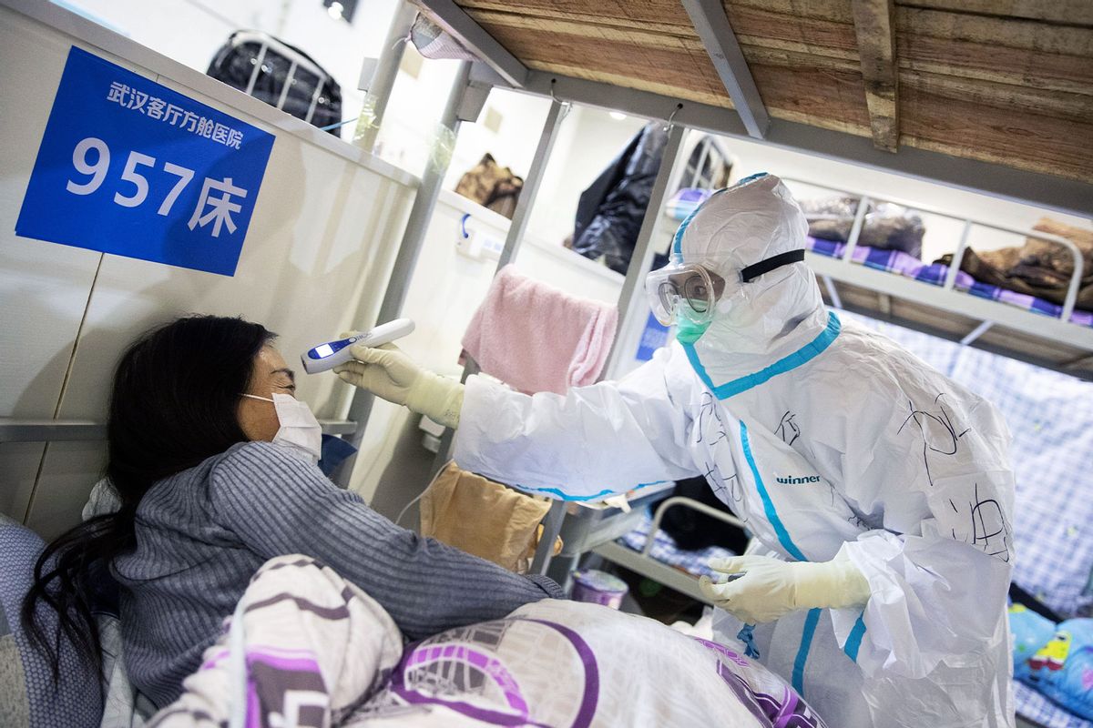 A member of the medical staff (L) checking the body temperature of a patient who has displayed mild symptoms of the COVID-19 coronavirus, at an exhibition centre converted into a hospital in Wuhan in China's central Hubei province. (STR/AFP via Getty Images)