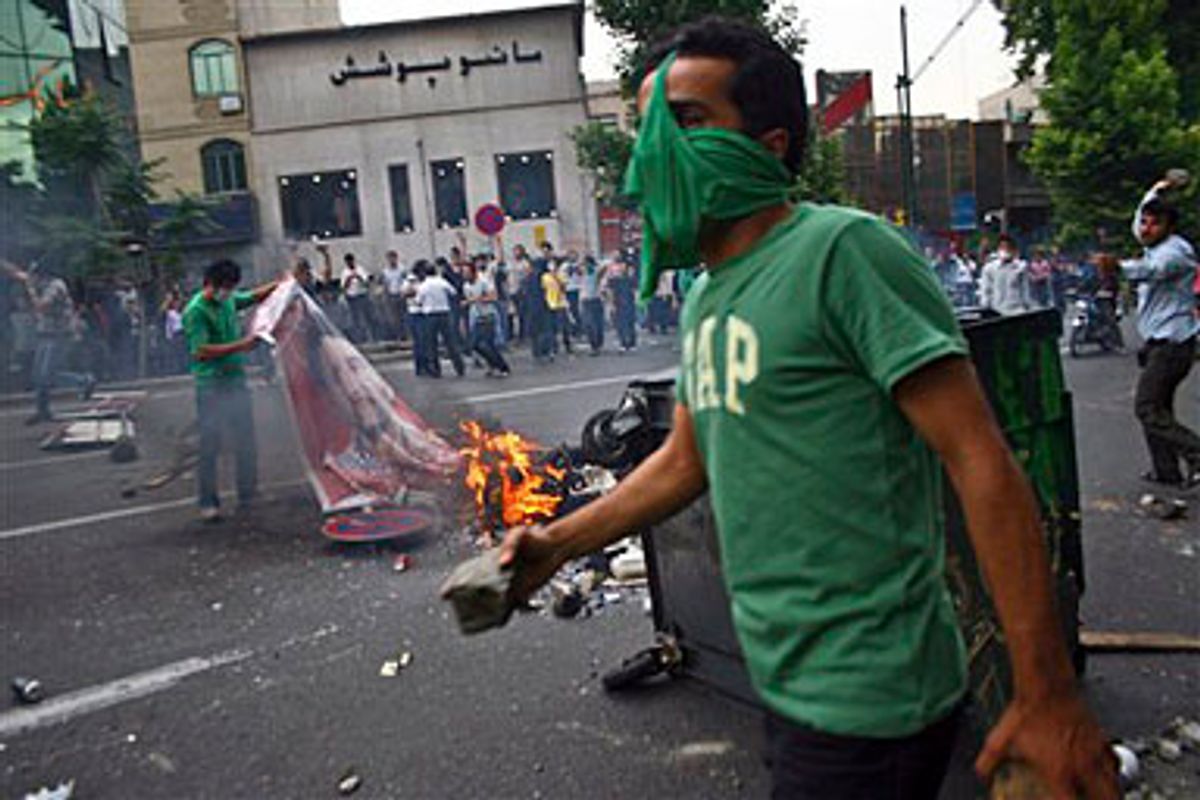 
A supporter of Iranian reformist presidential candidate, Mir Hussein Mousavi burns the poster of hard line president Mahmoud Ahmadinejad as others throw stones toward the security forces in Tehran, Saturday, June 13, 2009. 