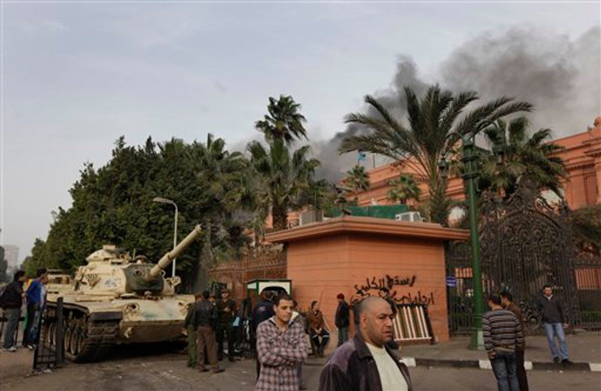An Egyptian army tank stands outside the Egyptian museum which remains intact,  right, as smoke billows in the background from the ruling National Democratic party building, torched by anti government protesters overnight, in central Cairo, Egypt, Saturday, Jan. 29, 2011. (AP Photo/Ben Curtis) (AP)