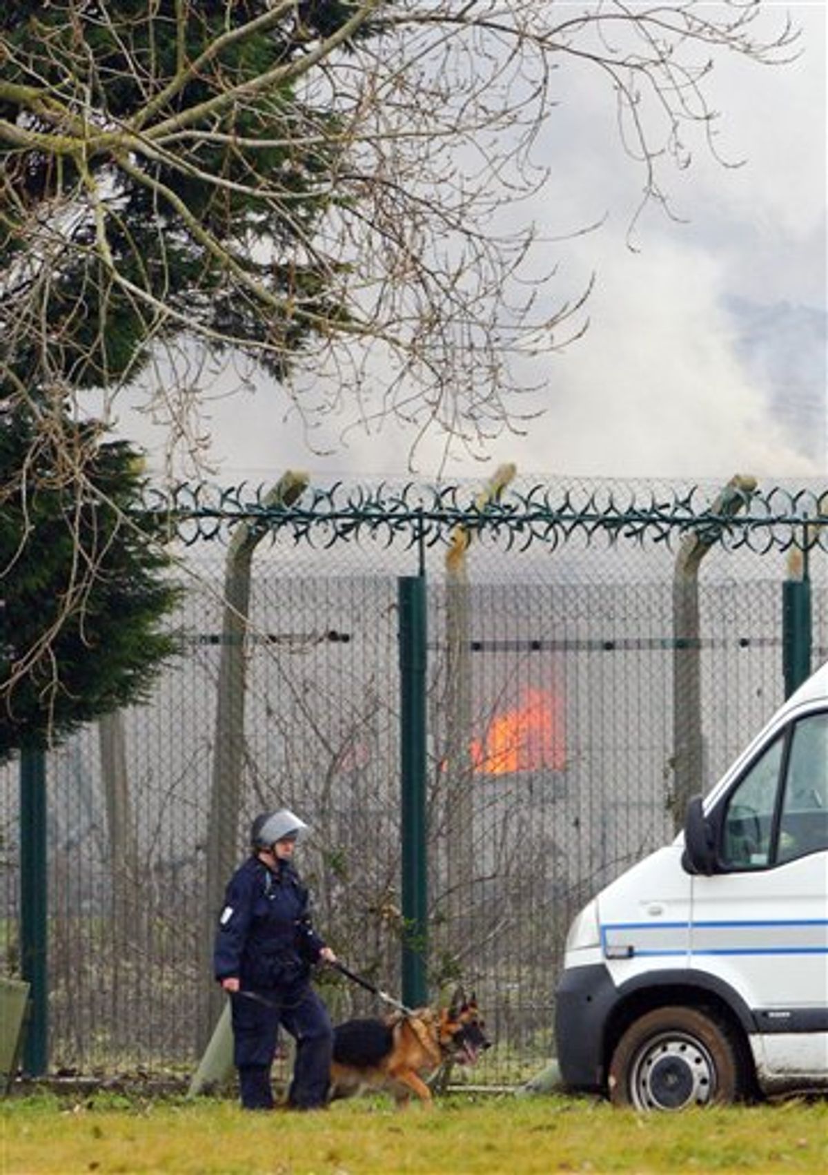 a specialist prison officer dog handler patrols outside the perimeter fence of Ford Prison near Arundel, south England, as the gymnasium building burns in background after about 40 prisoners began a riot and set alight to parts of the open prison, according to the a Ministry of Justice official, Saturday Jan. 1, 2011. (AP Photo / Chris Ison, PA) UNITED KINGDOM OUT - NO SALES - NO ARCHIVES  (AP)