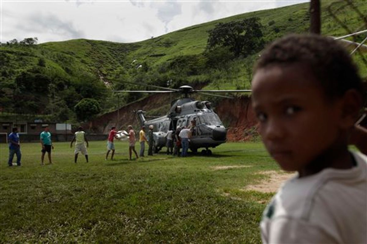 A boy looks on as residents unload supplies from an Navy helicopter at Sumidouro, an area isolated due to landslides in Teresopolis, Brazil, Tuesday, Jan. 18, 2011. Brazil's army on Monday sent some 700 soldiers to help throw a lifeline to desperate neighborhoods that have been cut off from food, water or help in recovering bodies since mudslides killed at least 665 people. (AP Photo/Felipe Dana) (AP)