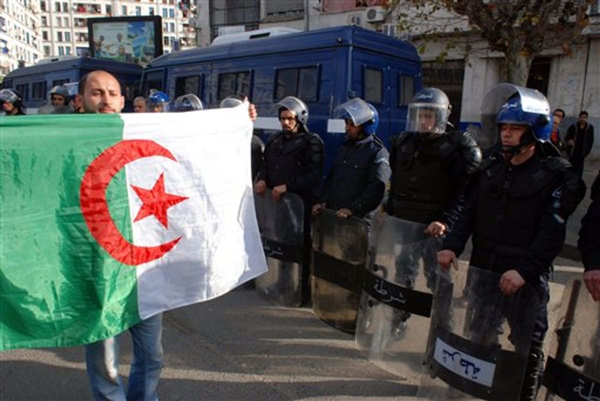 An Algerian protester holds an Algerian flag as he walks in front of Police officers during a demonstration in Algiers, Algeria, Saturday Feb. 12, 2011.  Some thousands of people defied a government ban on demonstrations and poured into the Algerian capital for a pro-democracy rally Saturday, a day after weeks of mass protests toppled Egypt's authoritarian leader. (AP Photo/Sidali  Djarboub) (AP)