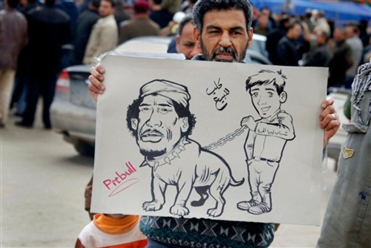 A protester holds a placard portraying Libyan Leader Moammar Gadhafi as a pitbull dog held on a chain by a youth, with writing in arabic reading "Dog for sale" and on arm of youth "Youth of Free Libya", in Benghazi, Libya Wednesday, Feb. 23, 2011. Militiamen loyal to Moammar Gadhafi clamped down in Tripoli Wednesday, but cracks in his regime spread elsewhere across the nation, as the protest-fueled rebellion controlling much of eastern Libya claimed new gains closer to the capital. (AP Photo/Alaguri) (AP)