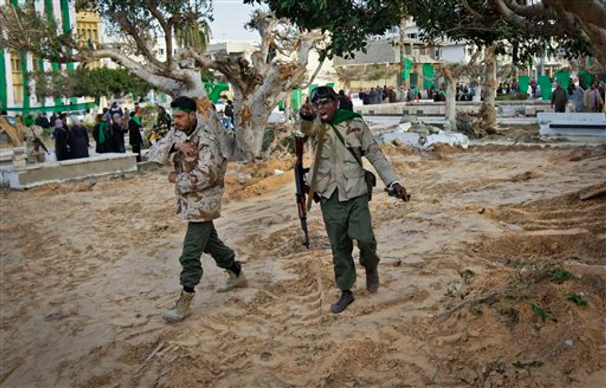 In this photo taken during a government-organised visit for foreign media, a pro-Gadhafi soldier mimics a gun with his hand as he and another walk across freshly-bulldozed ground from which the bodies of opposition dead had been exhumed, according to a resident, in the main square of Zawiya, Libya Friday, March 11, 2011. Libyan Leader Moammar Gadhafi's regime has gained momentum with the capture of Zawiya after days of fierce fighting with rebels, in a key test of the government's ability to maintain its hold on the Libyan capital and surrounding areas. (AP Photo/Ben Curtis) (AP)