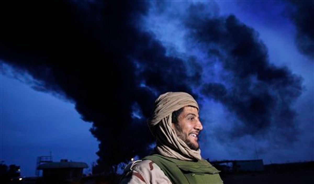 In this photo taken during a government-organised visit for foreign media, a pro-Gadhafi fighter is seen beneath a plume of smoke from the burning oil refinery in Ras Lanouf, 380 miles (615 kilometers) southeast of the capital Tripoli, in Libya Saturday, March 12, 2011. (AP Photo/Ben Curtis) (AP)