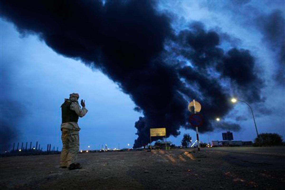 In this photo taken during a government-organised visit for foreign media, a pro-Gadhafi fighter makes his evening prayers in the desert as a plume of smoke rises from the burning oil refinery in Ras Lanouf, 380 miles (615 kilometers) southeast of the capital Tripoli, in Libya Saturday, March 12, 2011. (AP Photo/Ben Curtis) (AP)