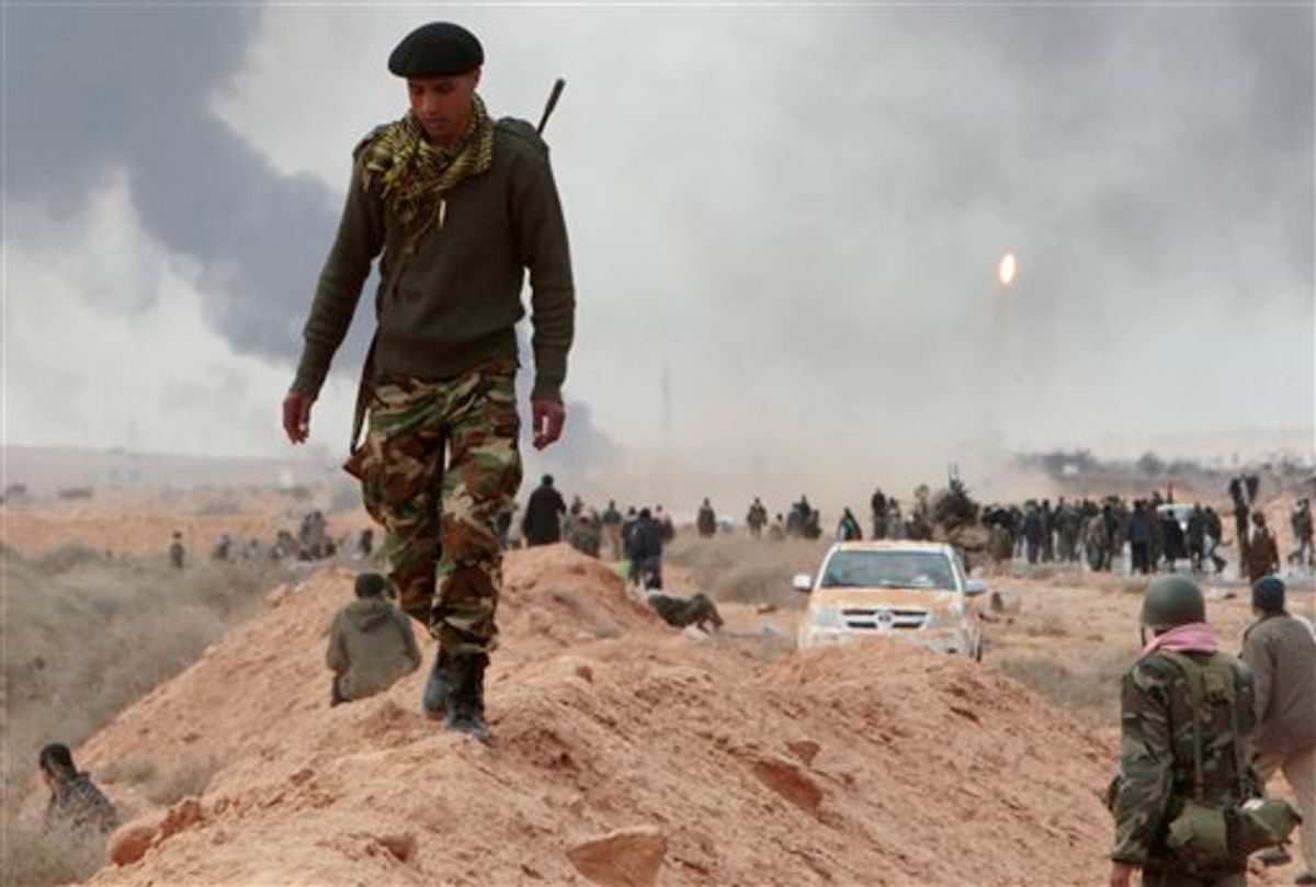 An anti-Gadhafi rebel, walks along a sand barrier, as other rebels fire a rocket launcher seen in the right, during  fighting against pro-Gadhafi fighters, in Sedra, eastern Libya, Wednesday March 9, 2011. A high-ranking member of the Libyan military flew to Cairo on Wednesday with a message for Egyptian army officials from Moammar Gadhafi, whose troops pounded opposition forces with artillery barrages and gunfire in at least two major cities. Gadhafi appeared to be keeping up the momentum he has seized in recent days in his fight against rebels trying to move on the capital, Tripoli, from territory they hold in eastern Libya. (AP Photo/Hussein Malla) (AP)