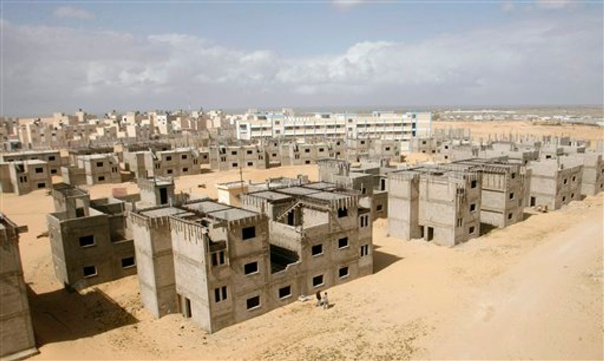 Palestinians pass by unfinished buildings at the UNRWA housing project in Khan Younis, southern Gaza Strip, Wednesday, March 9, 2011. Israel's military began transporting 40,000 tons of construction materials into the Gaza Strip at the Sufa Crossing on Wednesday, in a new move to ease its blockade of the coastal territory. The week-long operation will supply badly needed gravel for U.N. schools and other humanitarian projects, including homes in Khan Younis. (AP Photo/Eyad Baba) (AP)