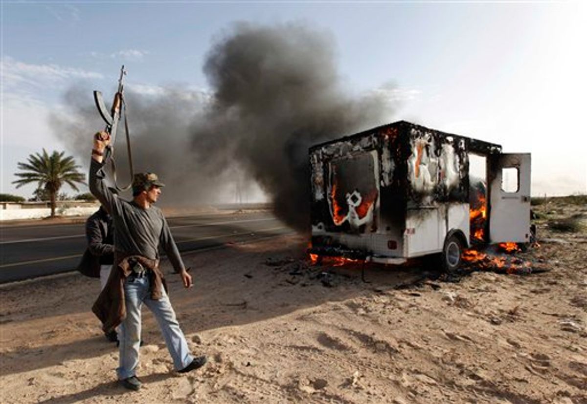 A Libyan rebel celebrates next to a burn pro-Moaamar Gadhafi fighters vehicle in the town of Brega, east of Libya, oWednesday March 2, 2011. Regime opponents battled forces loyal to Libyan leader Moammar Gadhafi who tried Wednesday to retake a key oil installation in a counteroffensive Wednesday against the rebel-held eastern half of the country. At one point in the flip-flopping battle, anti-Gadhafi fighters cornered the attackers in a nearby seaside university campus in fierce fighting that killed at least five. (AP Photo/Hussein Malla) (AP)