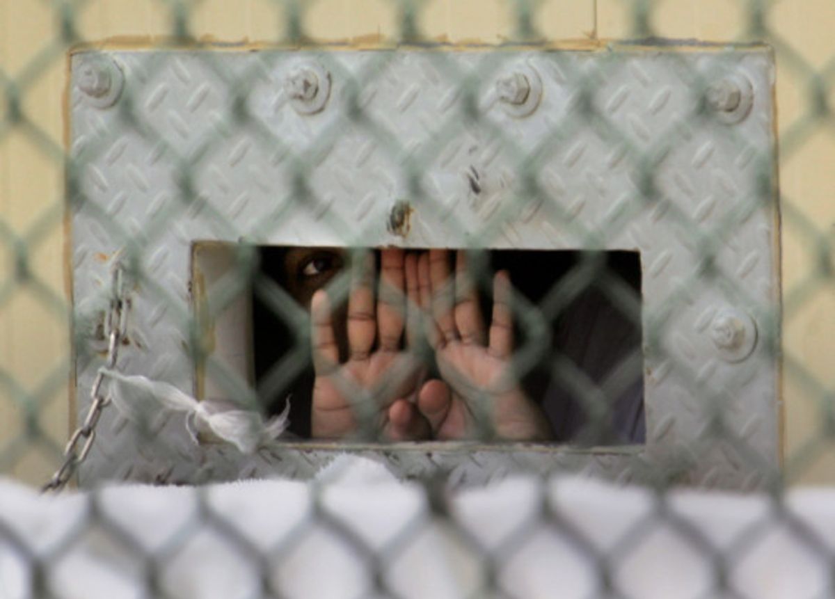 A detainee shields his face as he peers out through the so-called "bean hole" which is used to pass food and other items into detainee cells, at Camp Delta detention center, Guantanamo Bay U.S. Naval Base, Cuba, Monday, Dec. 4, 2006. 