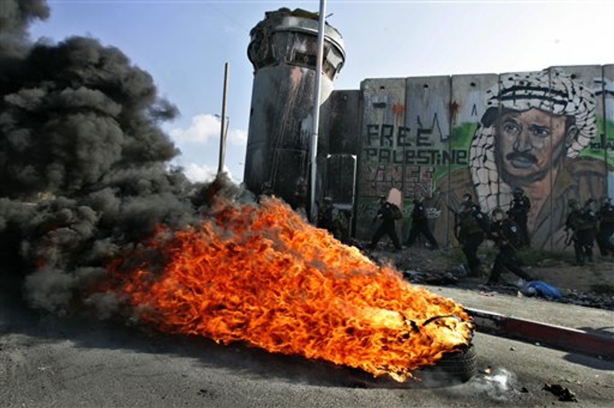 Israeli soldiers run past burning tires under a mural of the late Palestinian leader Yasser Arafat during clashes with Palestinian stone throwers following a protest to mark the upcoming 63rd anniversary of "Nakba", Arabic for "Catastrophe", the term used to mark the events leading to Israel's founding in 1948, in the Qalandia checkpoint between Ramallah and Jerusalem, Saturday, May 14, 2011.(AP Photo/Majdi Mohammed) (AP)