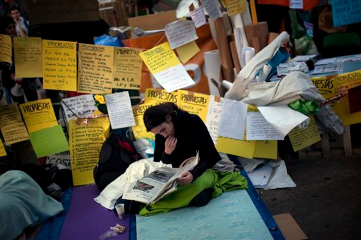 A demonstrator reads the newspaper as she spends the night in Sol square during a protest in Madrid. (AP/Emilio Morenatti)   