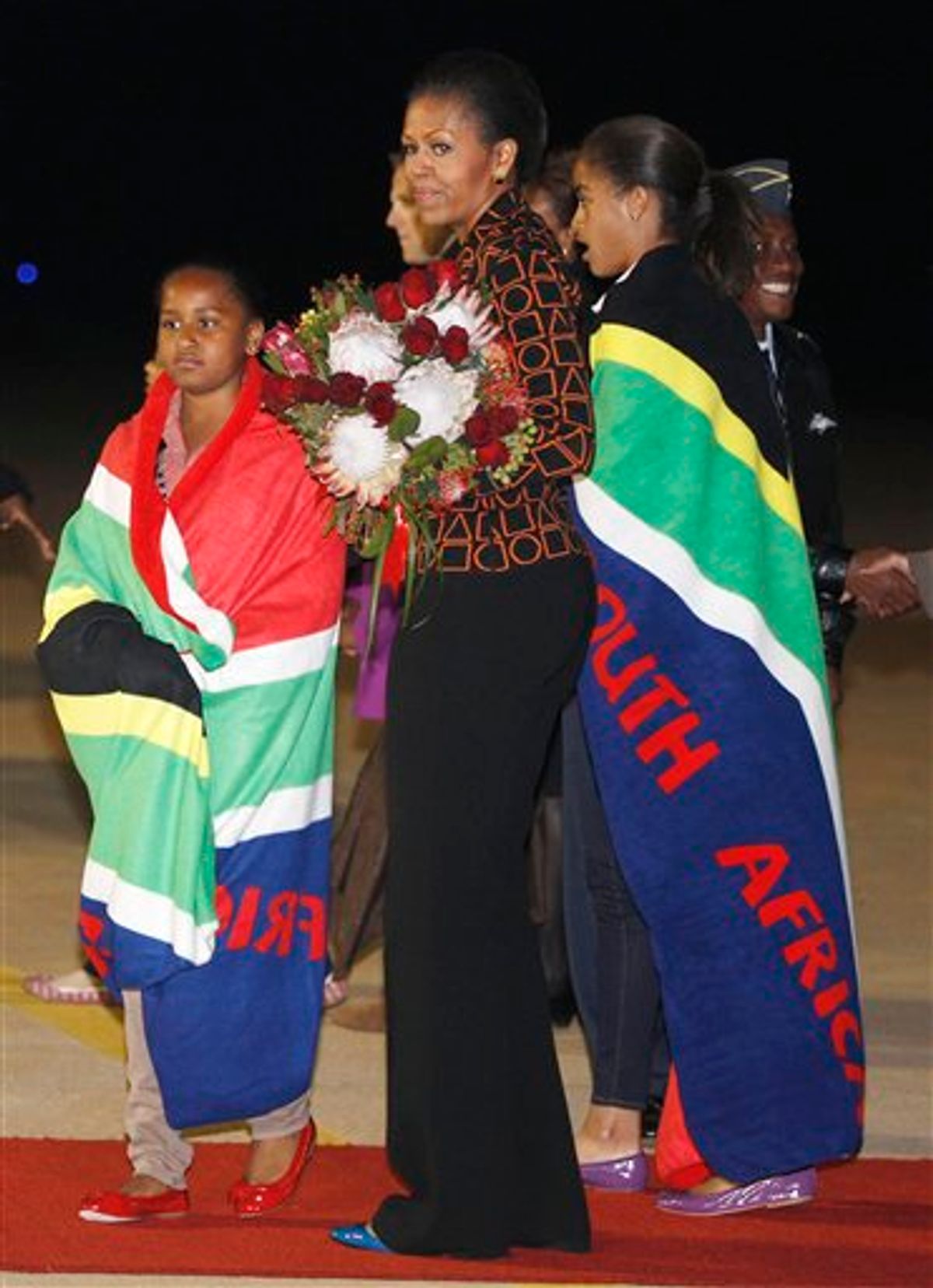 First lady Michelle Obama holds a bouquet of flowers, and daughters Malia, right, and Sasha, are draped in blankets given to them upon landing in Pretoria, en route to Johannesburg, South Africa, Monday, June 20, 2011, as they begin their week long trip to Africa. (AP Photo/Charles Dharapak, Pool)  (AP)