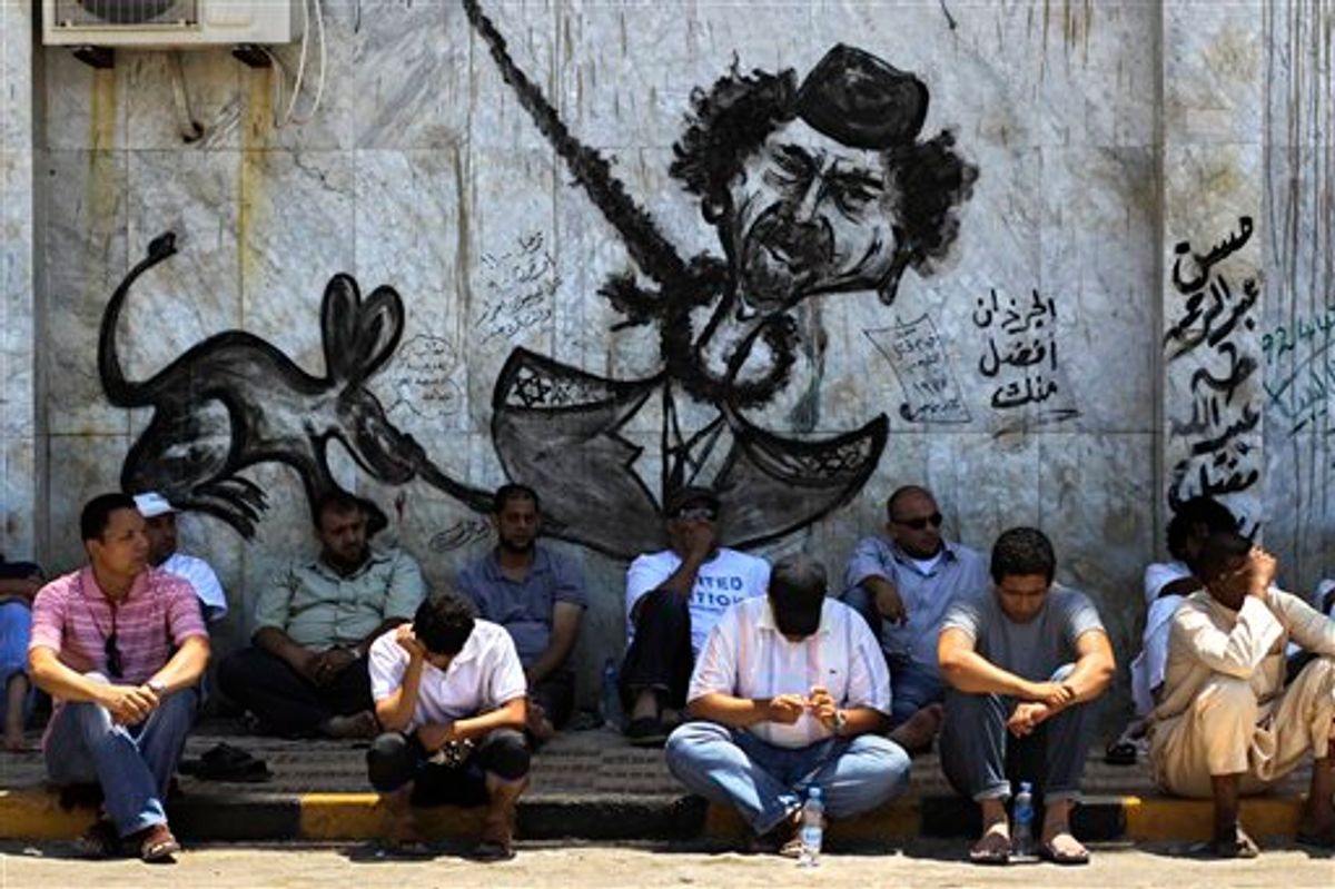 LIbyans sit in the shade under a graffiti depicting Libyan dictator Moammar Gadhafi before a Friday prayer in rebel-held Benghazi, Libya, Friday, July 8, 2011. NATO denied a Libyan government charge Thursday that the alliance is intentionally using its airstrikes to assist rebel advances, saying it is sticking to its mandate to protect civilians. (AP Photo/Sergey Ponomarev) (AP)