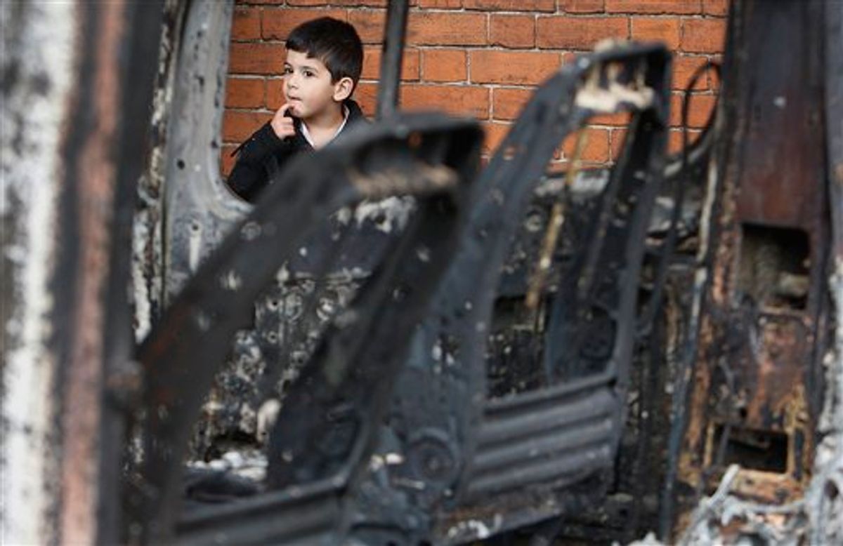 A unidentified boy reacts behind a burned car in Tottenham, north London, Sunday, Aug. 7, 2011 after a demonstration against the death of a local man turned violent and cars and shops were set ablaze. One police officer was hospitalized and seven others were injured during riots after a north London suburb exploded in anger Saturday night following a gathering to protest the Thursday shooting by police of the 29-year-old. (AP Photo/Akira Suemori) (AP)
