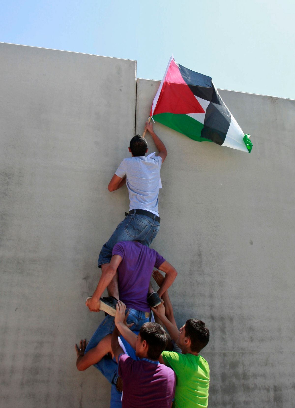 A Palestinian holding a national flag climbs the separation barrier during a protest against its construction in the West Bank village of Walajeh, outside Jerusalem. Friday, Sept. 16, 2011. (AP Photo/Nasser Shiyoukhi) (Associated Press)