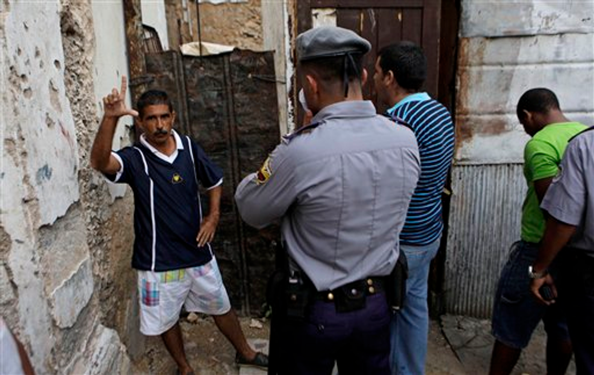 A dissident signs the letter "L" for the Spanish word "libertad" or freedom as he is detained by police during a procession celebrating Cuba's patron saint in Havana, Cuba, Thursday Sept. 8, 2011
