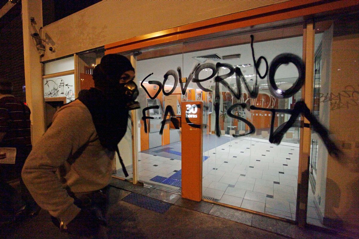 A demonstrator wearing a gas mask walks past a a bank covered by the words in Portuguese "Fascist government" at a protest against an increase in price for public transportation in Sao Paulo, Brazil, Thursday, June 13, 2013.     (AP/Nelson Antoine)