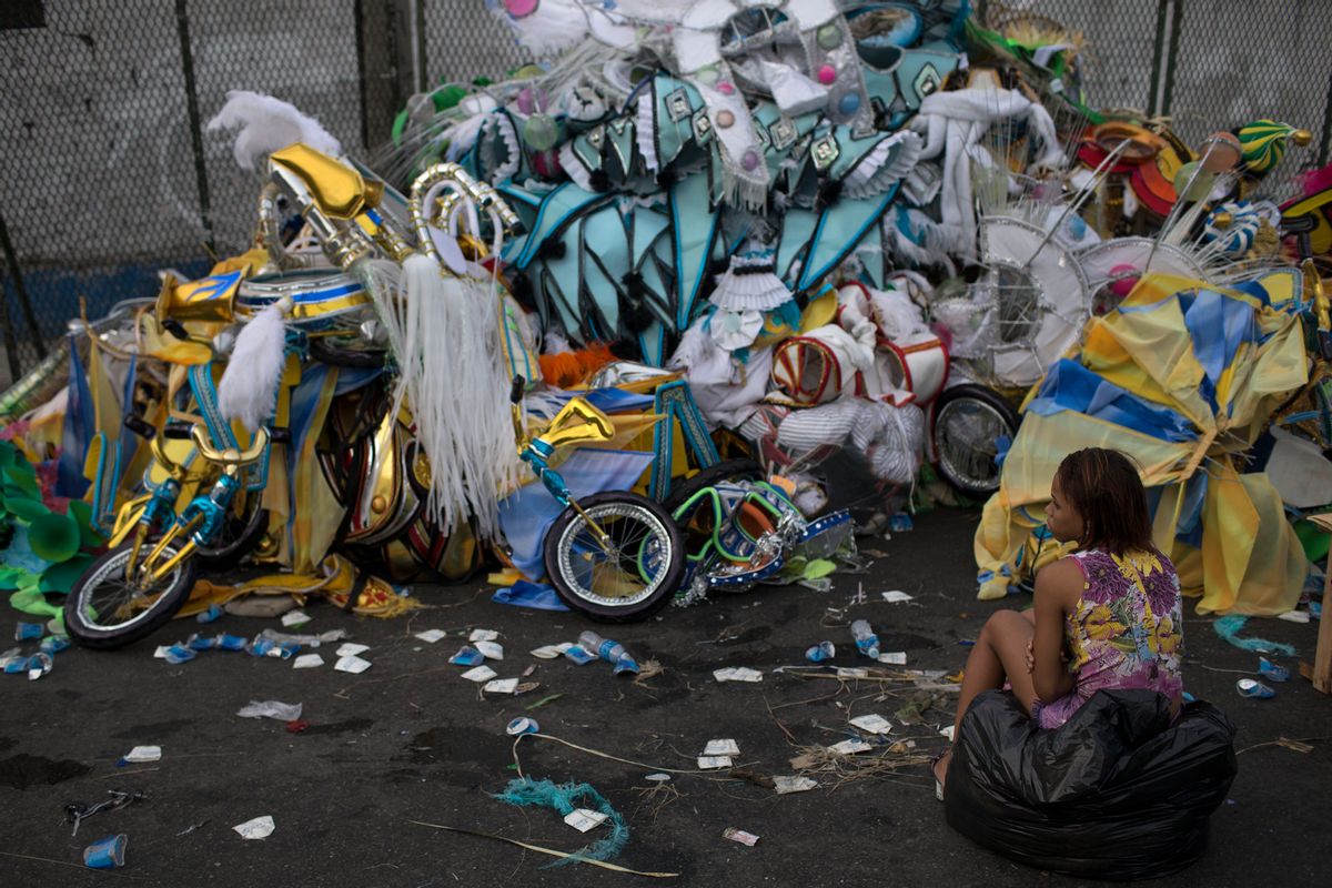 A woman sits in front of a pile of discarded carnival costumes after carnival celebrations at the Sambadrome in Rio de Janeiro, Brazil, Tuesday, March 4, 2014. The costumes on display at the all-night parade that ended early Tuesday have made Rioís Carnival celebration the most famous in the world. But the handmade confections often have a short shelf life. As the tens of thousands of revelers stream out of the Sambadrome, a surprising number of them immediately abandon their costumes. (AP Photo/Felipe Dana)
