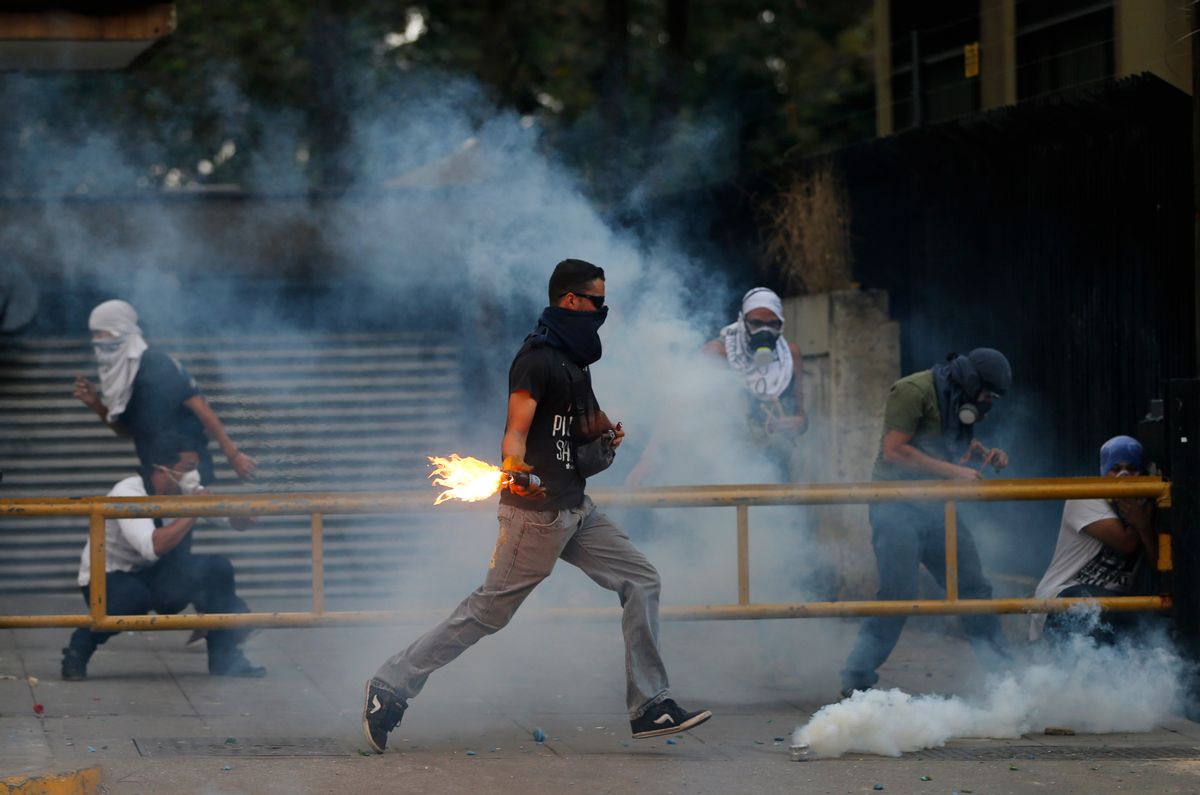 A demonstrator runs to throw a molotov bomb against Bolivarian National Police officers during clashes in Caracas, Venezuela, Thursday, March 6, 2014.   (AP/Fernando Llano)