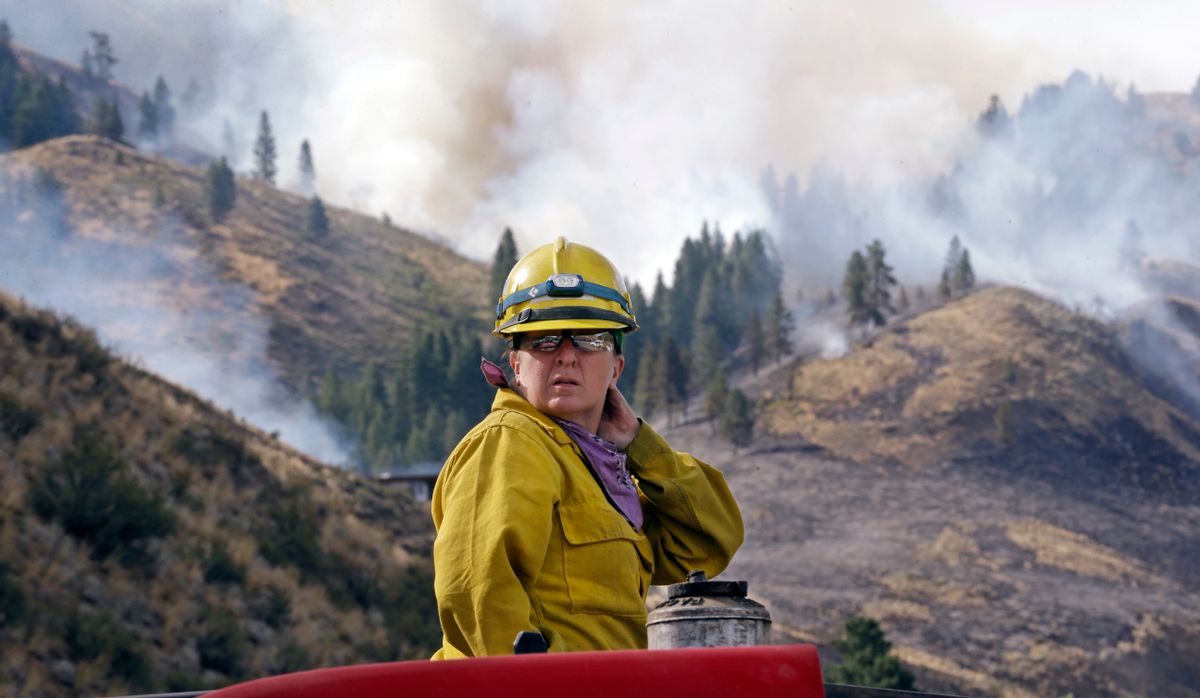 Firefighter Kathleen Calvin looks around as she sits atop her fire truck while waiting to begin work as smoke from a wildfire fills the sky behind Saturday, July 19, 2014, in Winthrop, Wash. (AP Photo/Elaine Thompson)  