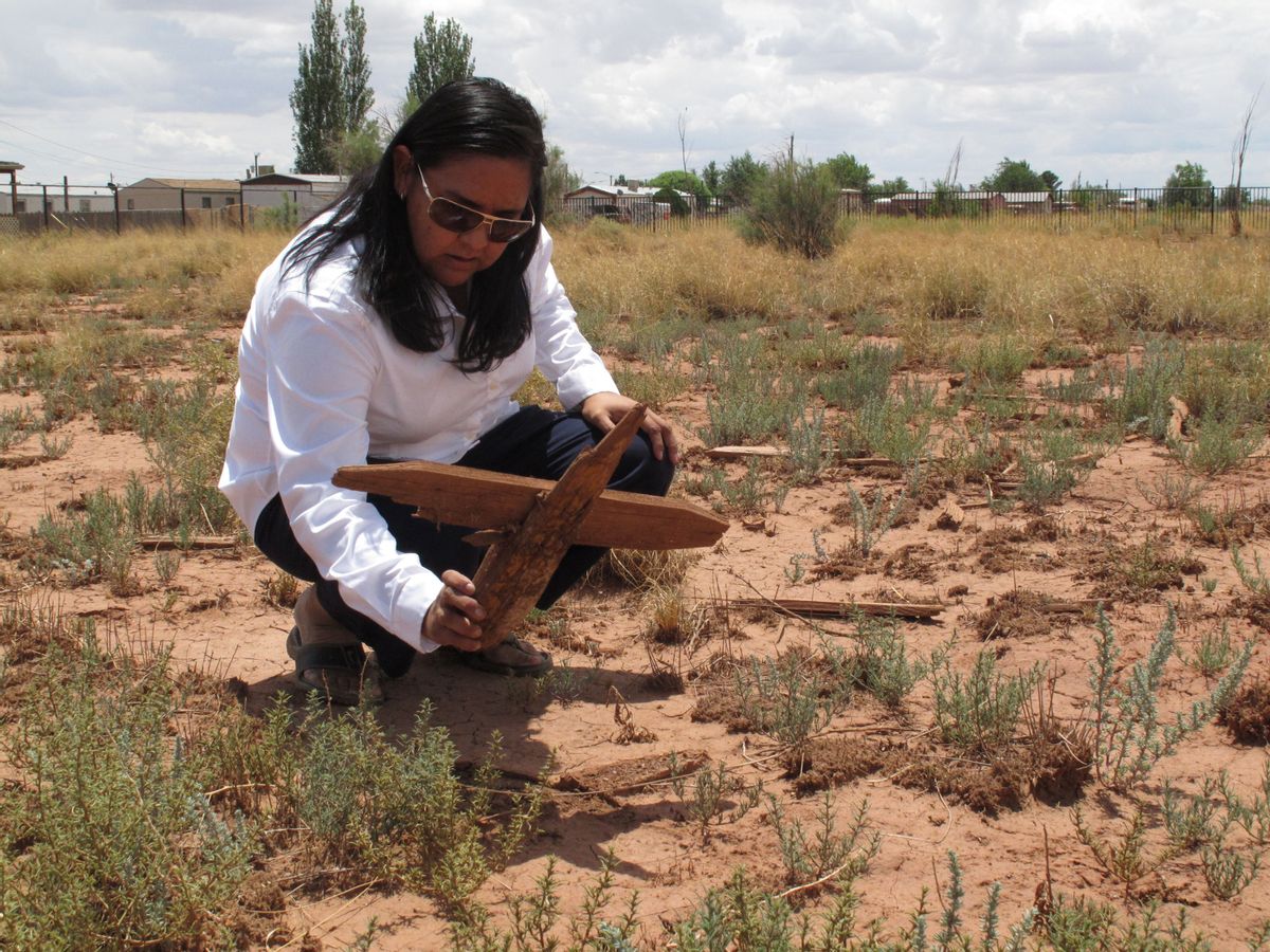 This July 9, 2014 photo shows Navajo archaeologist Kim Mangum picking up a wooden cross at a cemetery in Winslow, Arizona. Local historic preservation Commissioner Gail Sadler has made it her mission to unearth the identities of roughly 600 people buried there and help their descendants reconnect with a lost part of their history. (AP Photo/Felicia Fonseca) (AP)