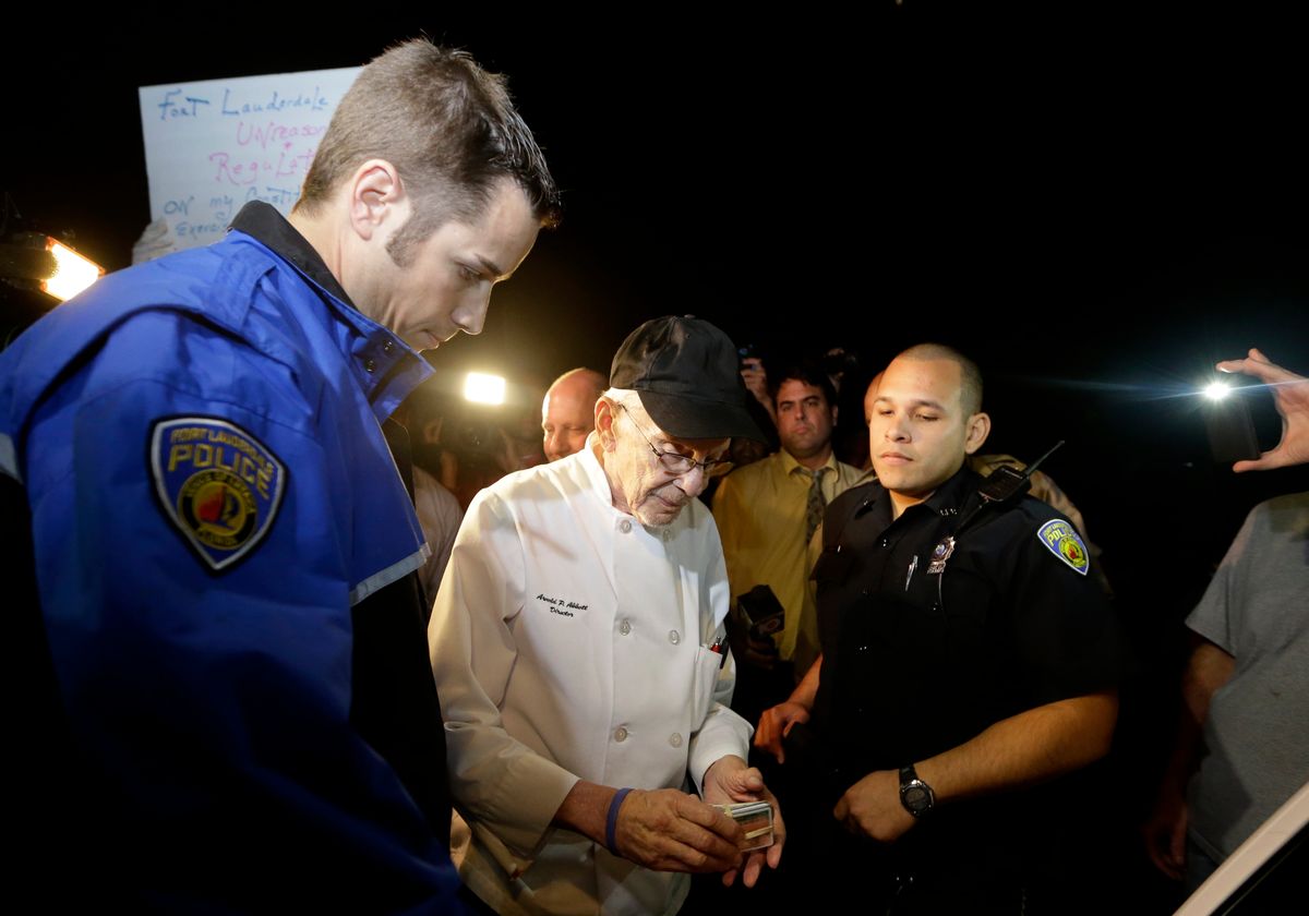 Homeless advocate Arnold Abbott, 90, of the nonprofit group Love Thy Neighbor Inc., center, gets his drivers license to hand to a  Fort Lauderdale police officer, Wednesday, Nov. 5, 2014, in Fort Lauderdale, Fla. Abbott and a group of volunteers were feeding the homeless in a public parking lot next to the beach when he was issued a summons to appear in court for violating an ordinance that limits where charitable groups can feed the homeless on public property.  Abbott w also recently arrested along with two pastors for feeding the homeless in a Fort Lauderdale park. (AP Photo/Lynne Sladky) (AP)